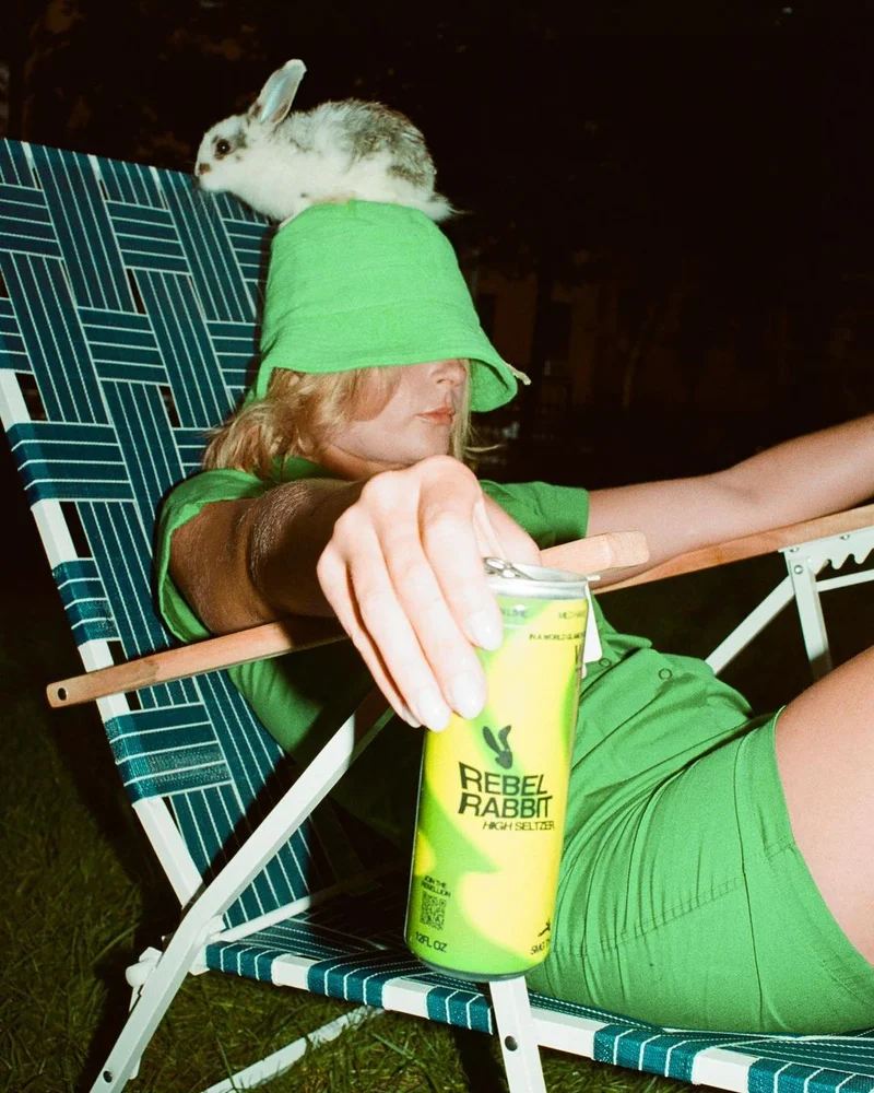 Girl in all green outfit, sitting down with a Mild Hare Lemon Lime and a rabbit on her head