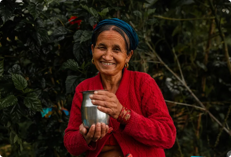 A Nepalese woman holds a cup of clean water while smiling.