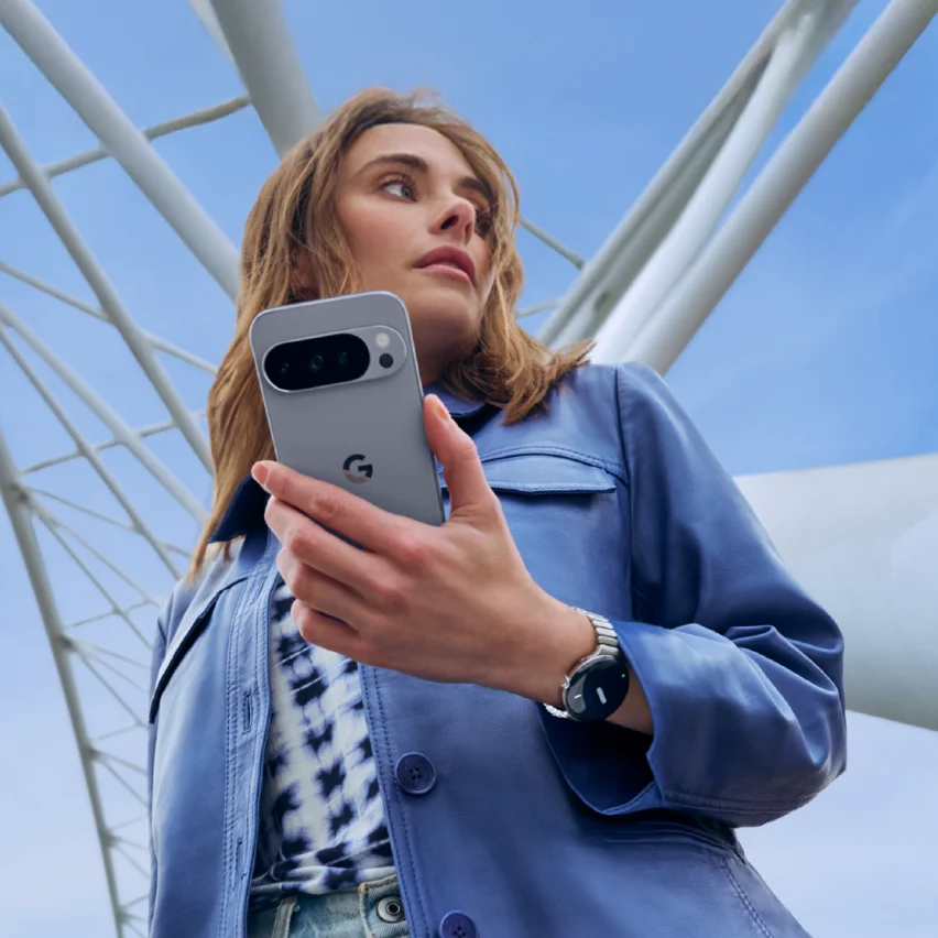 A woman in a blue leather jacket holding a gray Google Pixel phone and wearing a smartwatch.