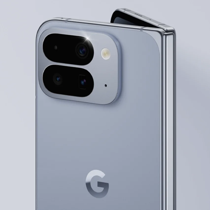 A close-up shot of the back of a light blue Google Pixel Fold smartphone, with a dual-lens camera bar and flash. The phone is slightly ajar, showing its hinge mechanism. The Google G logo is visible below the camera bar.