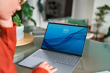 Over-shoulder view of a person working on a Dell AI 16 Plus laptop computer at home.