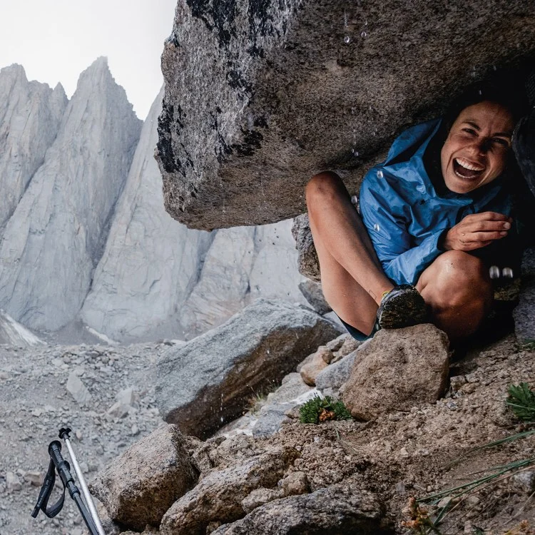 Patagonia. A hiker laughs as she squeezes beneath a rock outcropping to get out of the rain.