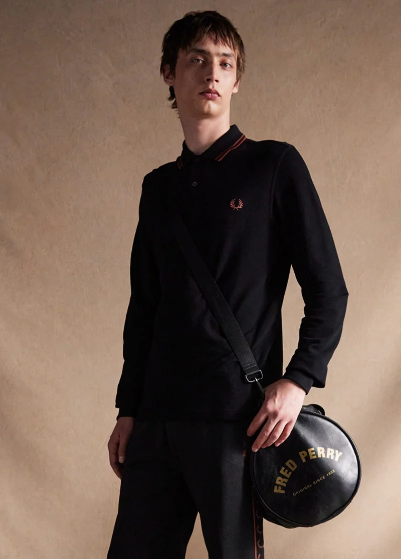 Model wears a Fred Perry Shirt and carries our black barrel bag