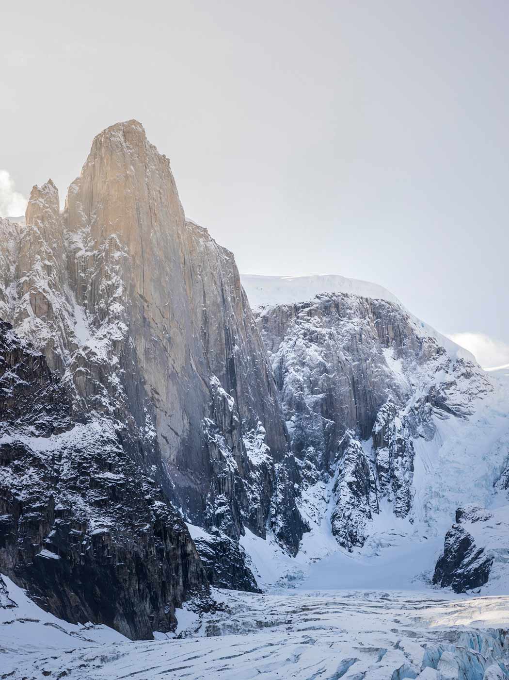 Photo of a sheer rock wall rising high out of a glacier.