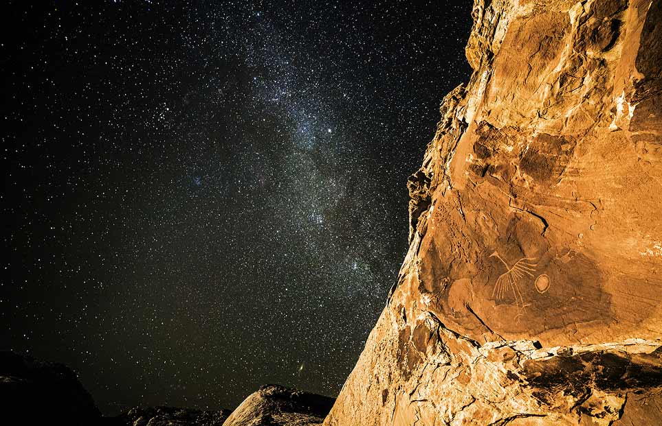 Photo of a petroglyph on a rock wall beneath the Milky Way.