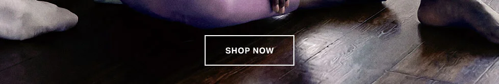 Woman in cozy purple loungewear sitting on a wooden floor with a 'SHOP NOW' button. Explore our new comfortable athleisure collection.