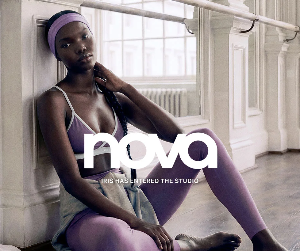 Iris, a woman in Nova purple sports bra, leggings, and headband, sits relaxed in a bright studio, promoting comfortable activewear.