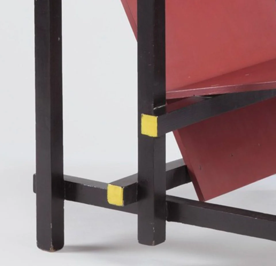 A close-up of a chair with dark blue legs and a red seat