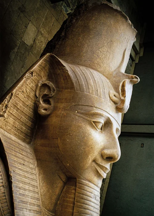 The head of Ramses II’s recumbent colossus at Memphis wears the nemes, or striped head cloth, and the royal uraeus serpent of divinity and authority.