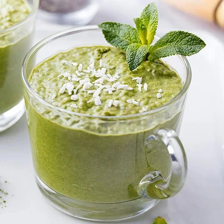 A close-up of a green chia pudding garnished with shredded coconut and a mint sprig.