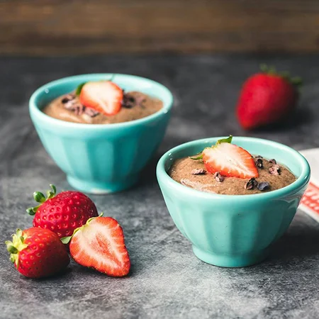 An elegant shot of two teal bowls filled with chia chocolate pudding, garnished with strawberry halves and cacao nibs.