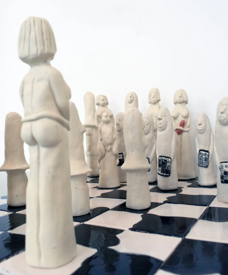Close-up of ceramic chess pieces with unique human-like forms on a chessboard.