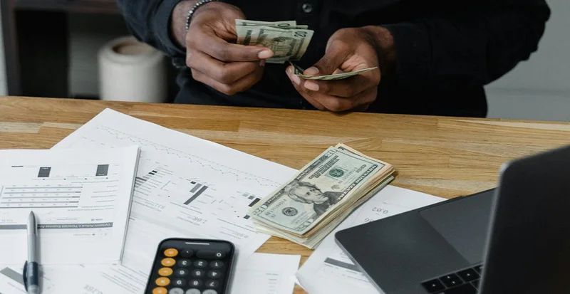 Person counting cash at a table with bills, calculator, and financial documents