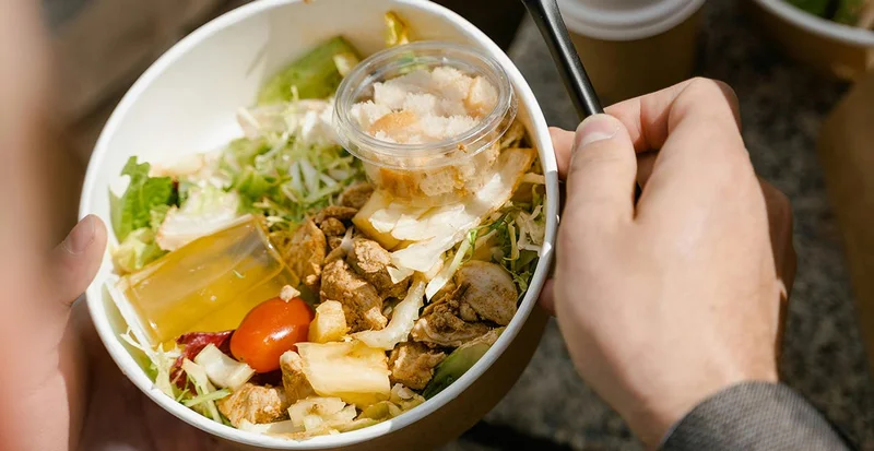 Close-up of a takeaway salad with chicken, vegetables, and dressing