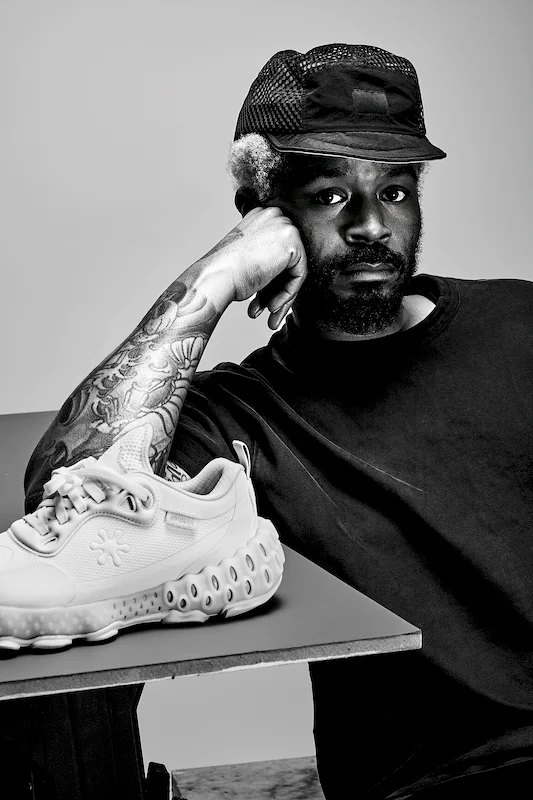 A black-and-white portrait of a man posing with a sneaker on a table
