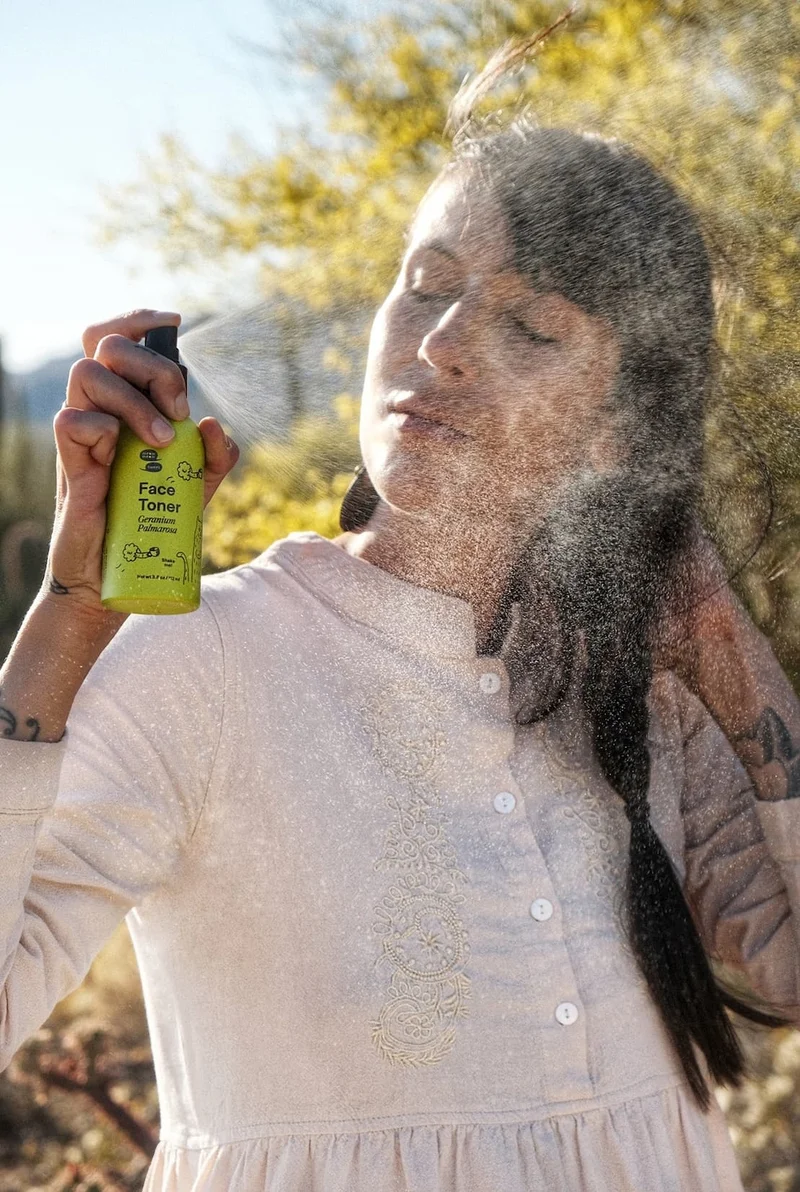 A tan-skinned person with a white dress sprays toner into the sunbeams