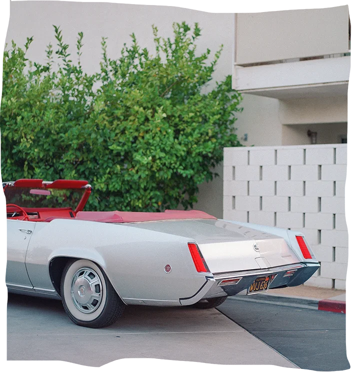 Vintage convertible with shiny silver exterior and red interior parked beside a modern building.