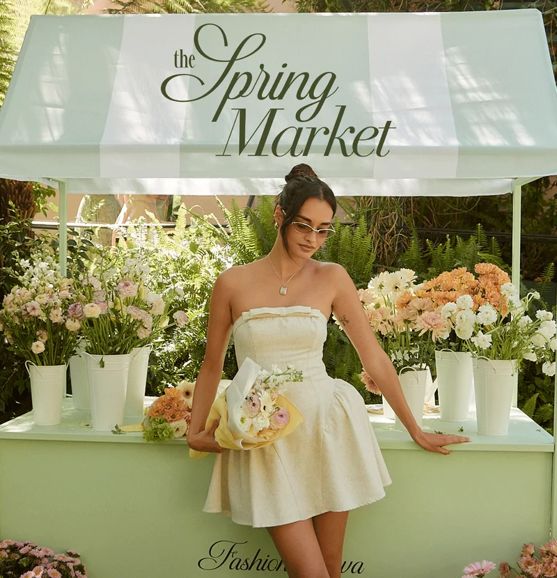 Woman in a chic cream strapless mini dress by a vibrant "Spring Market" flower stall. Explore the latest spring fashion collection.
