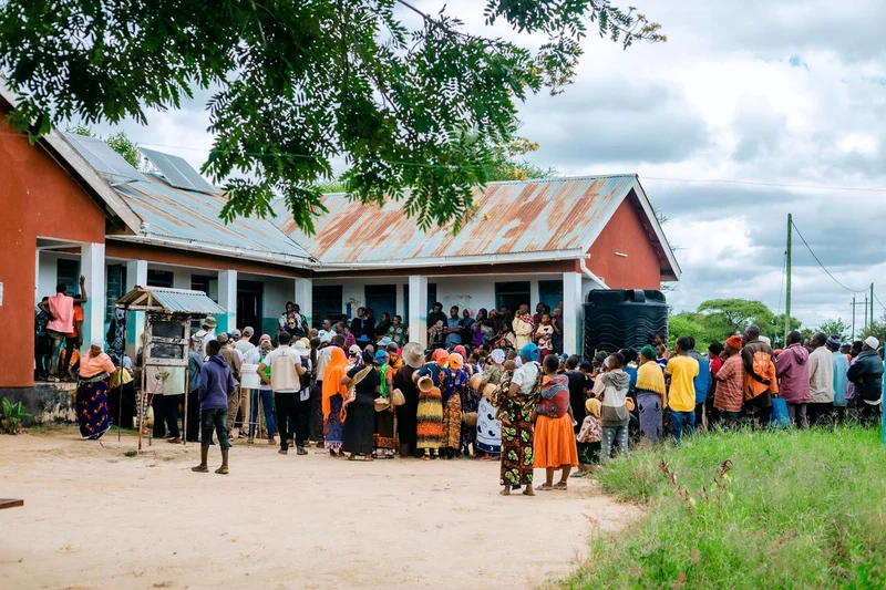 Community members in Tanzania and charity: water staff gathered around a building.
