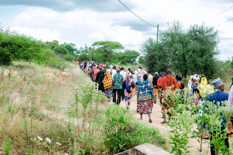 Community members in Tanzania walk alongside charity: water staff down a path.