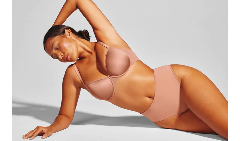 A tanned woman in a nude colored bra and panties, posing from the side.