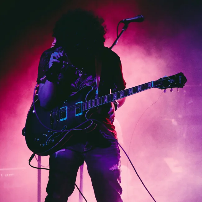 Silhouette of a man performing with a guitar on stage.