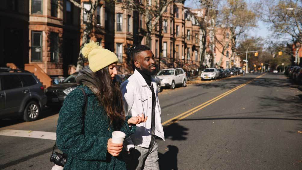 Image description: Two people walking through a New York City neighborhood with brownstones.