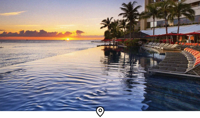 Image Description: Landscape view of the oceanside infinity pool at Sheraton Waikiki Beach Resort, with a fiery sunset in the background