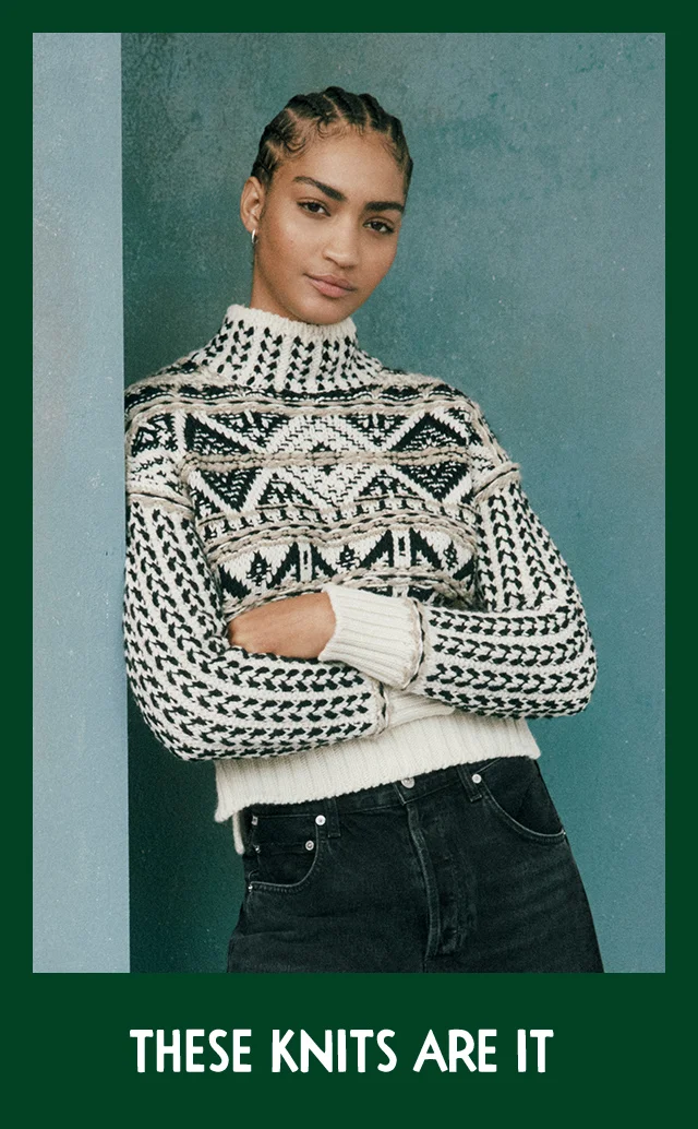 A woman wearing a patterned turtleneck sweater with black jeans.