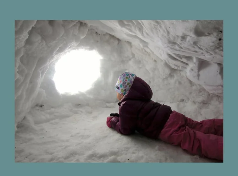 A kid peers out of a snow cave.