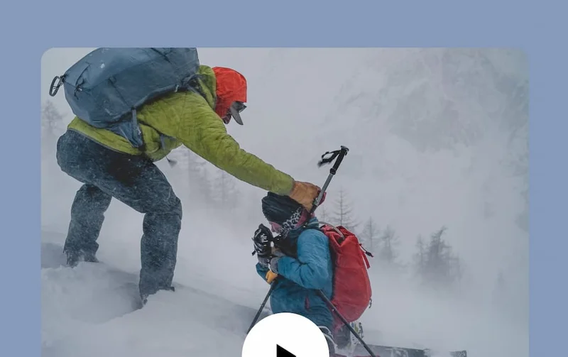 A grown-up helps a kid get their hood up during a blizzard.