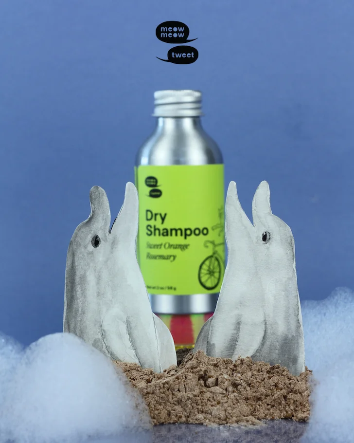 A metal bottle with a green label is placed between two paper cut-out dolphins.