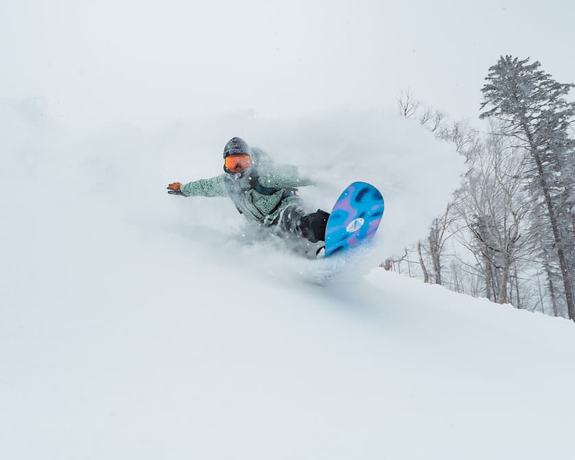 Snowboarder riding [ak] Outerwear and Family Tree Snowboard in powder