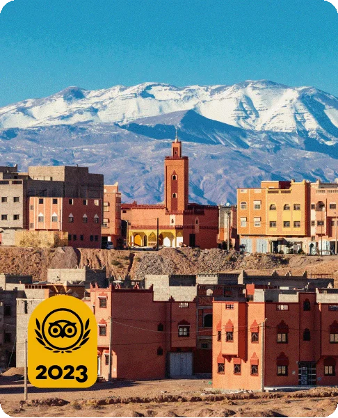 Image Description: Two levels of tan and orange-hued buildings with a towering snow-capped mountain range in the background. A Travelers’ Choice Awards Best of the Best yellow logo is in the bottom left corner.