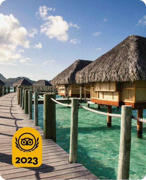 Image Description: Wooden walking bridge framed by clear, turquoise waters and rows of overwater bungalows. A Travelers’ Choice Awards Best of the Best yellow logo is in the bottom left corner.