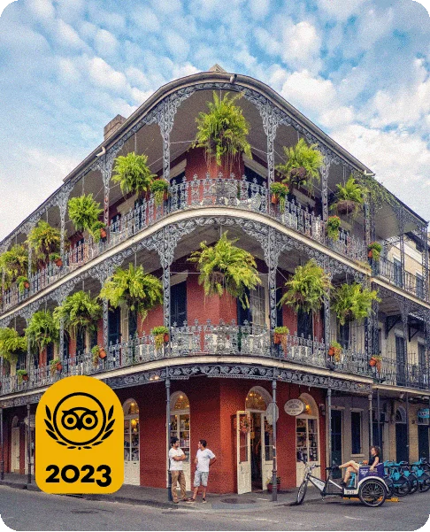 Image Description: Two people stand talking on a street corner with a pedicab driver waiting beneath an ornate multi-level building with wraparound terraces and hanging plants. A Travelers’ Choice Awards Best of the Best yellow logo is in the bottom left corner.