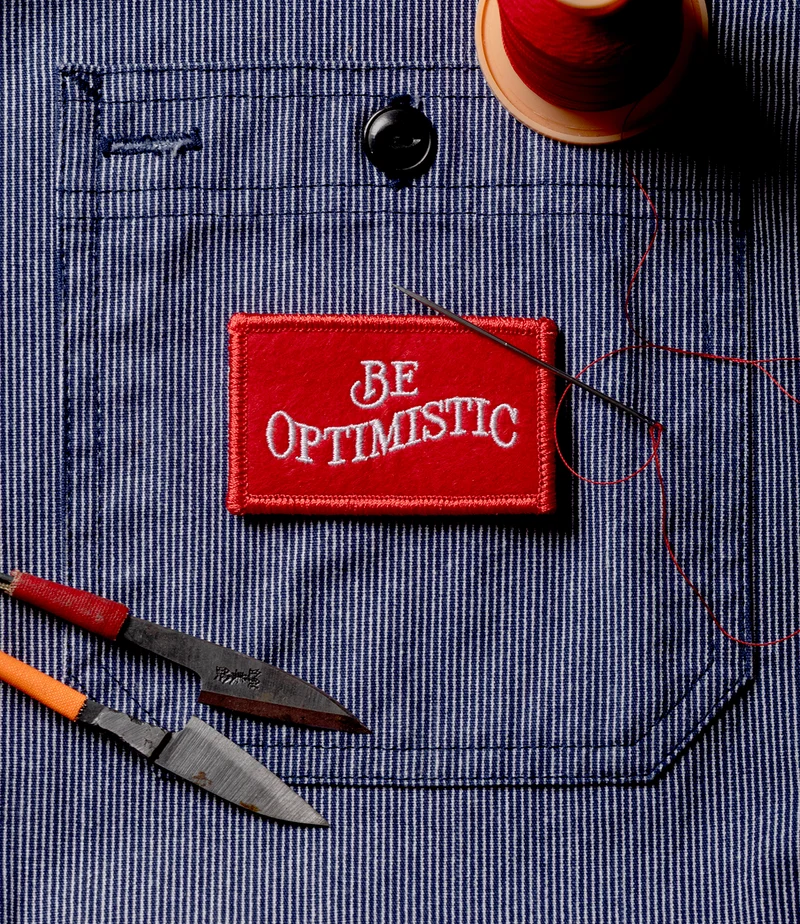 an image of a red patch with the words be optimistic on it