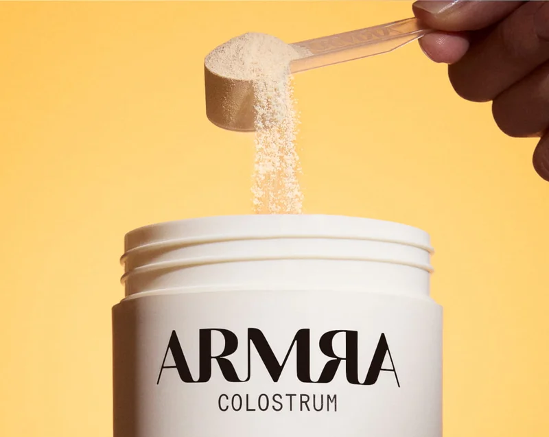 Scoop of powdered supplement being poured into an open ARMRA container.