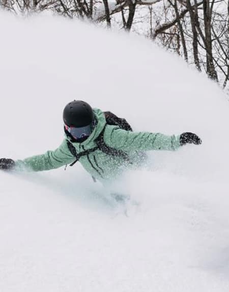 Snowboarder in a mint green jacket carving through powder with "All-Day Missions" text.
