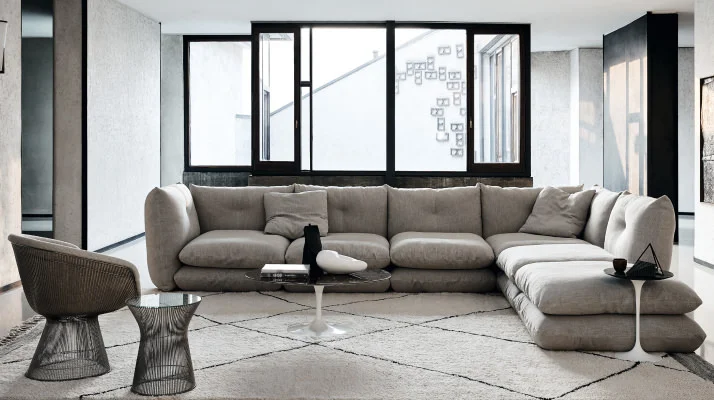 A modern room with white walls and black accents featuring a gray Perron Pillo Sofa in L Shaped sectional  on the right and a Planter Chair and Side Table facing it from the left.