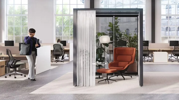 An open, brightly lit space with brick walls and floor-to-ceiling windows featuring Knoll Rockwell Unscripted Creative Walls, Saarinen Side Tables, burnt-orange lounge chairs, and lighting from Design Within Reach