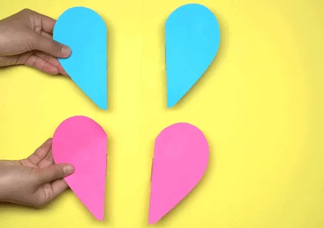 Hands holding two blue magnetic heart pieces that come together to form a complete heart. Yellow background.
