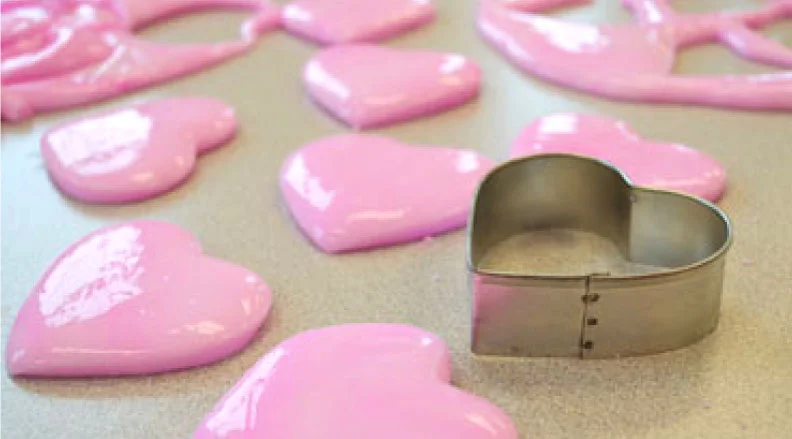 Close-up of pink, heart-shaped flubber pieces on a flat surface with a heart-shaped cookie cutter.