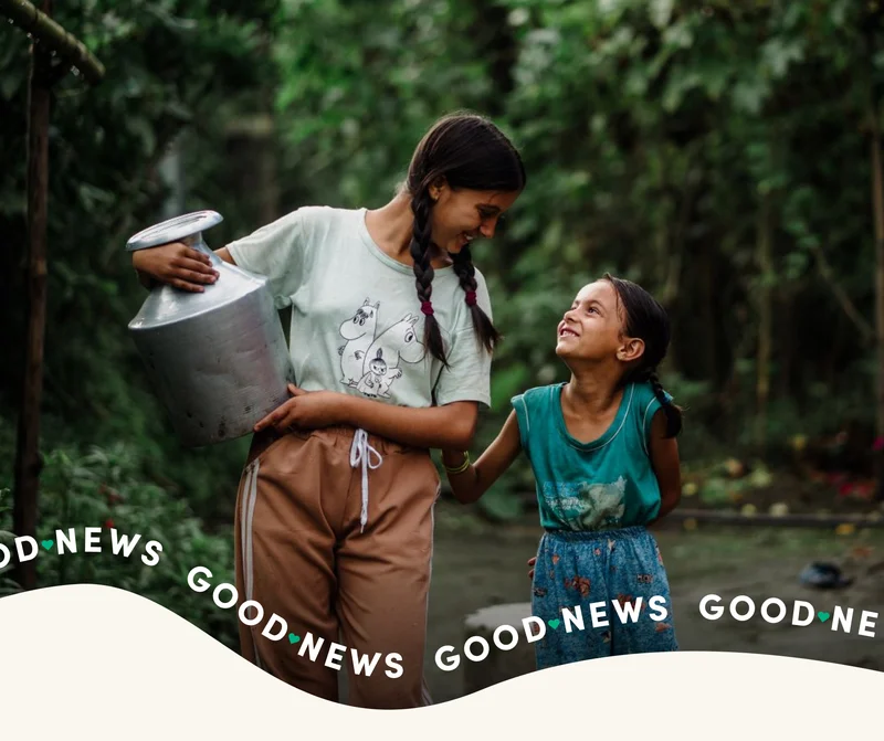 Two girls smile at each other as they walk back with clean water.