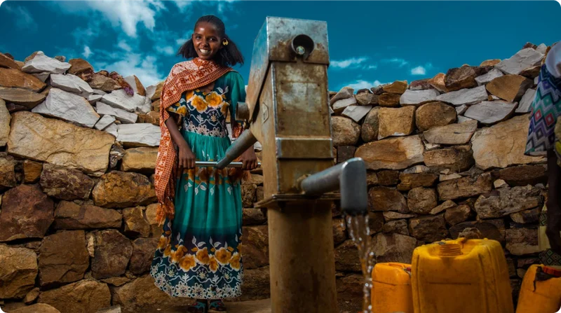 A woman smiles at the camera as she pumps clean water.