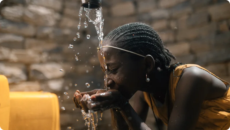 A girl drinks water out of a tap stand.