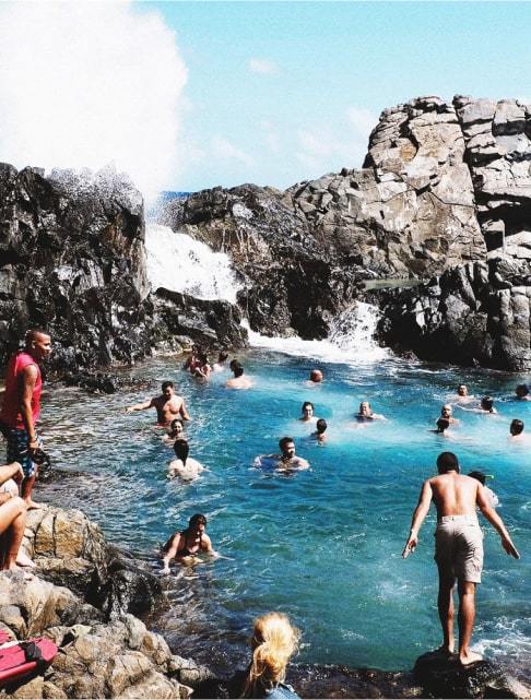 Image Description: Travelers enjoying a dip by the sea at the Conchi Natural Pool in Arikok National Park, Aruba