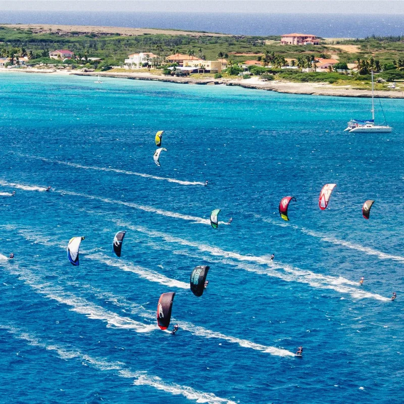 Image Description: Aerial view of kitesurfers sailing across the clear blue waters of Malmok Beach, Aruba