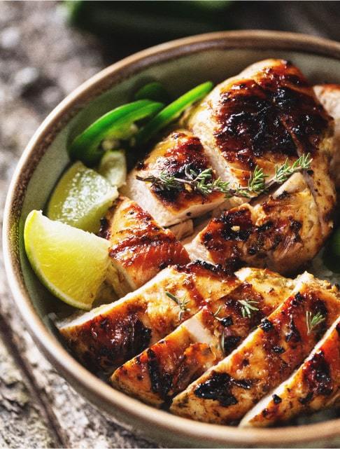 Image Description: Close-up of a bowl of Caribbean jerk chicken with sliced limes and jalapenos