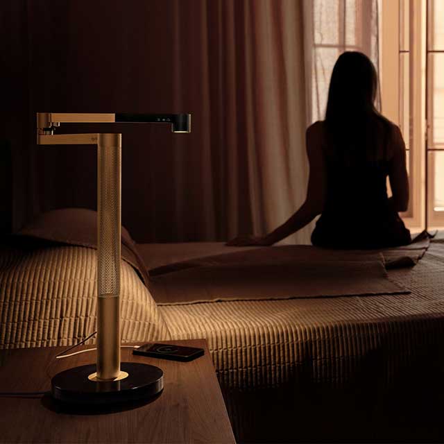 Owner sat on the edge of her bed with the Dyson Solarcycle Morph desk light on her bedside table.